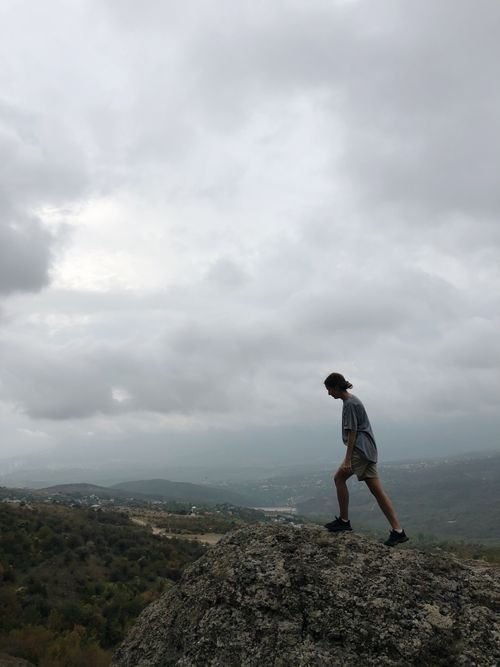 Free Side view of anonymous hiker walking on rocky hilltop under cloudy sky in mountainous valley Stock Photo