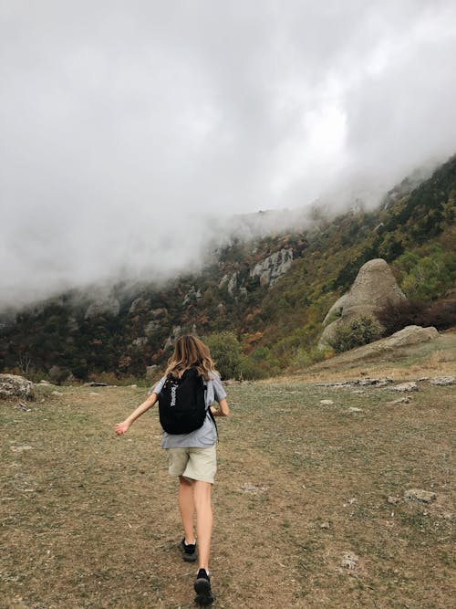 Unrecognizable female hiker walking on hill slope against foggy sky in wild valley