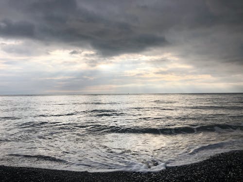 Peaceful scenery of waving foamy endless ocean washing stony coast against dramatic sunset sky