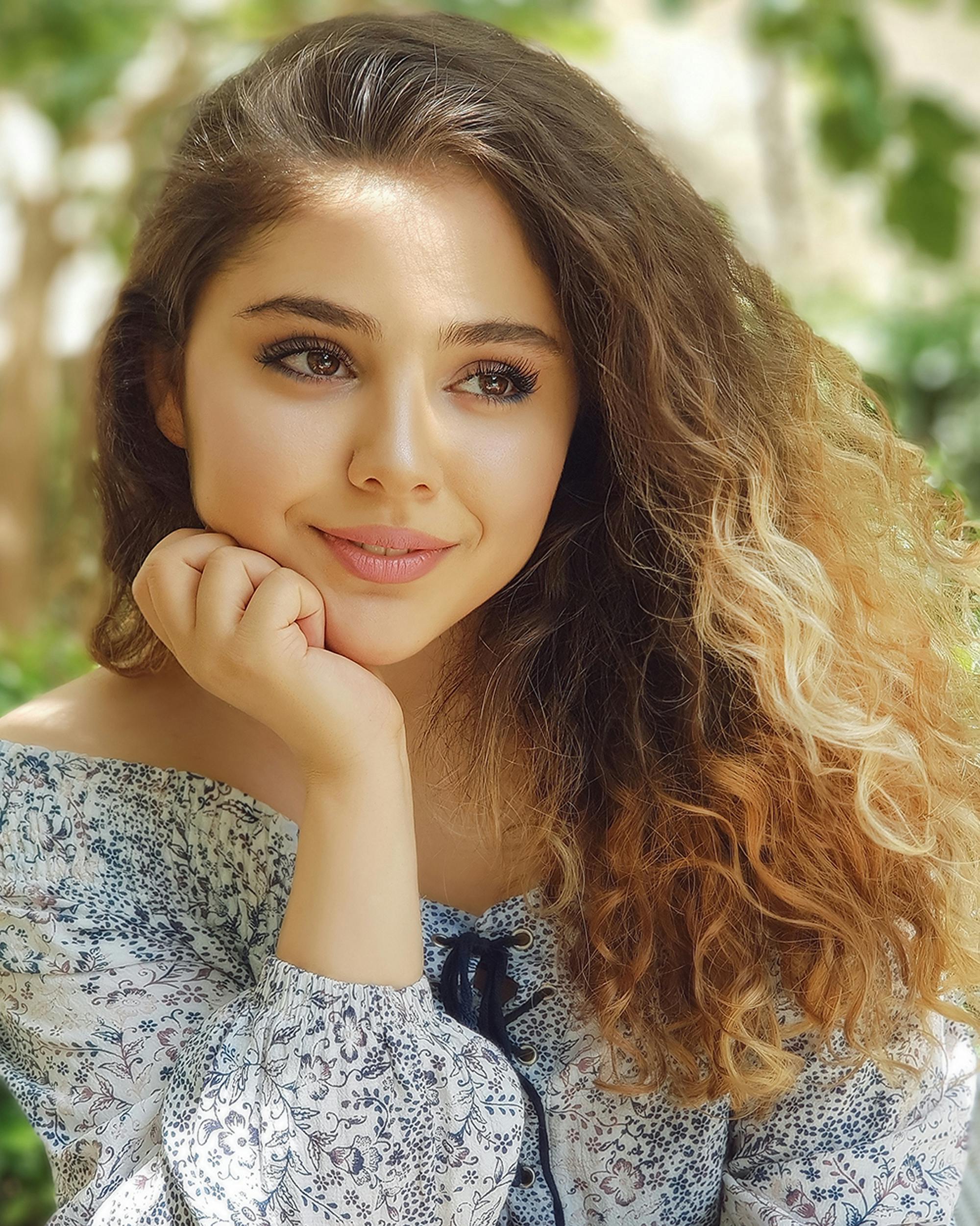 Portrait of a smiling woman with curly hair posing in an outdoor setting in Tehran, Iran.