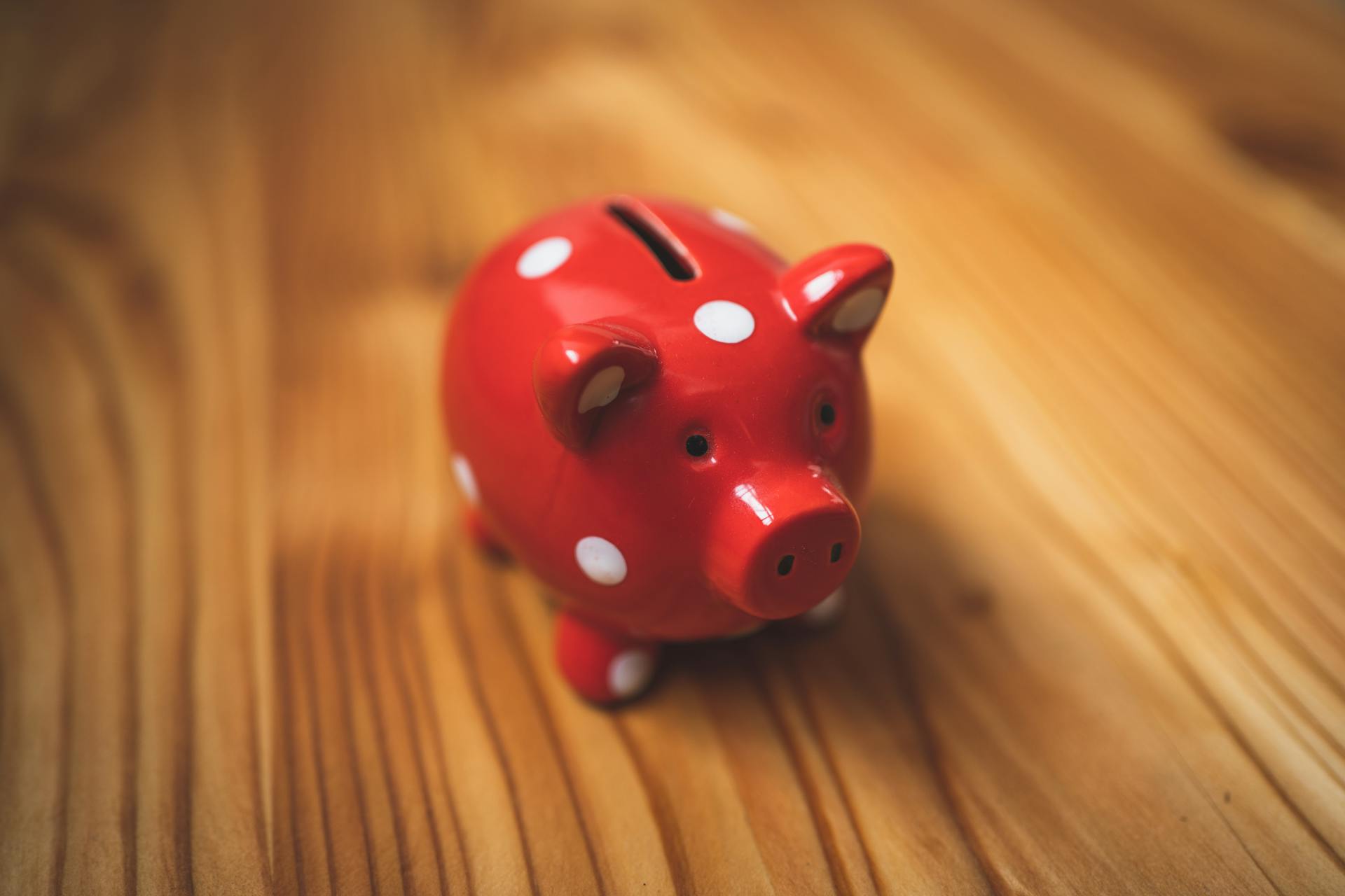 Close-up of a red polka dot piggy bank on a wooden surface, symbolizing savings.