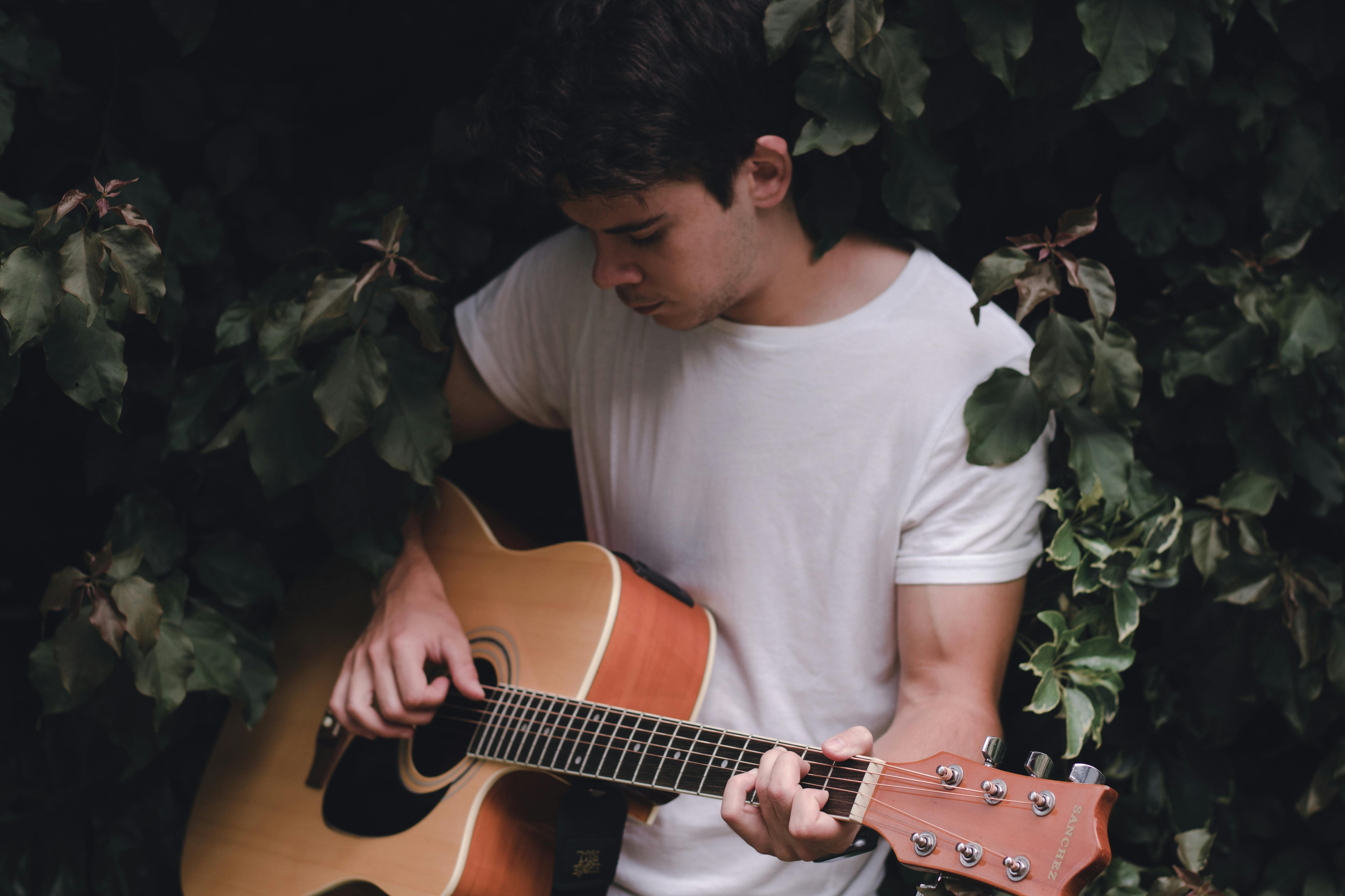 focused guitarist playing guitar sitting among green leaves