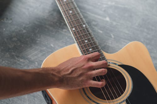 High angle of crop anonymous male guitarist touching acoustic guitar while practicing melody