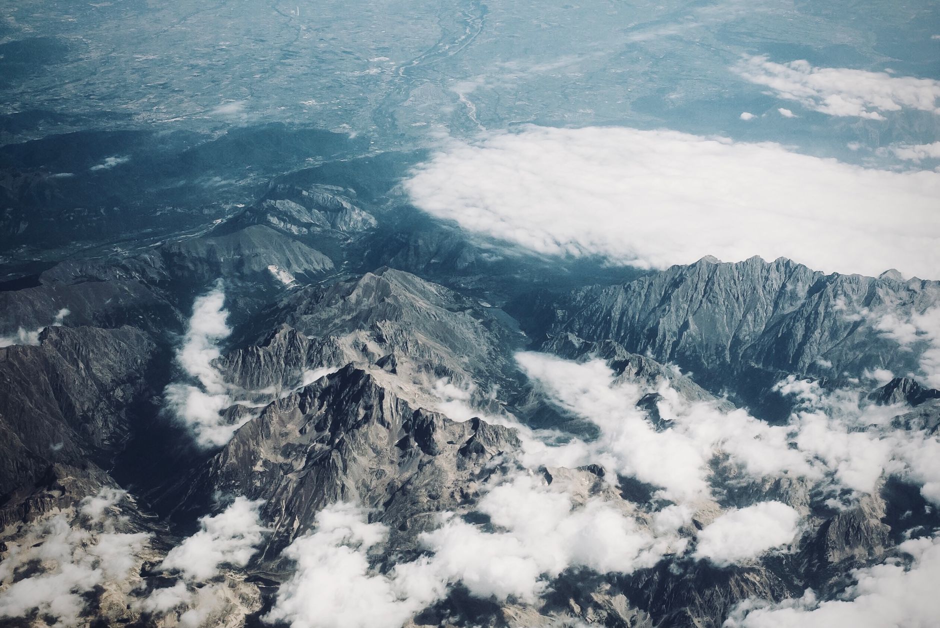 Drone shot of rugged mountain peaks covered by drifting clouds in a vast landscape.