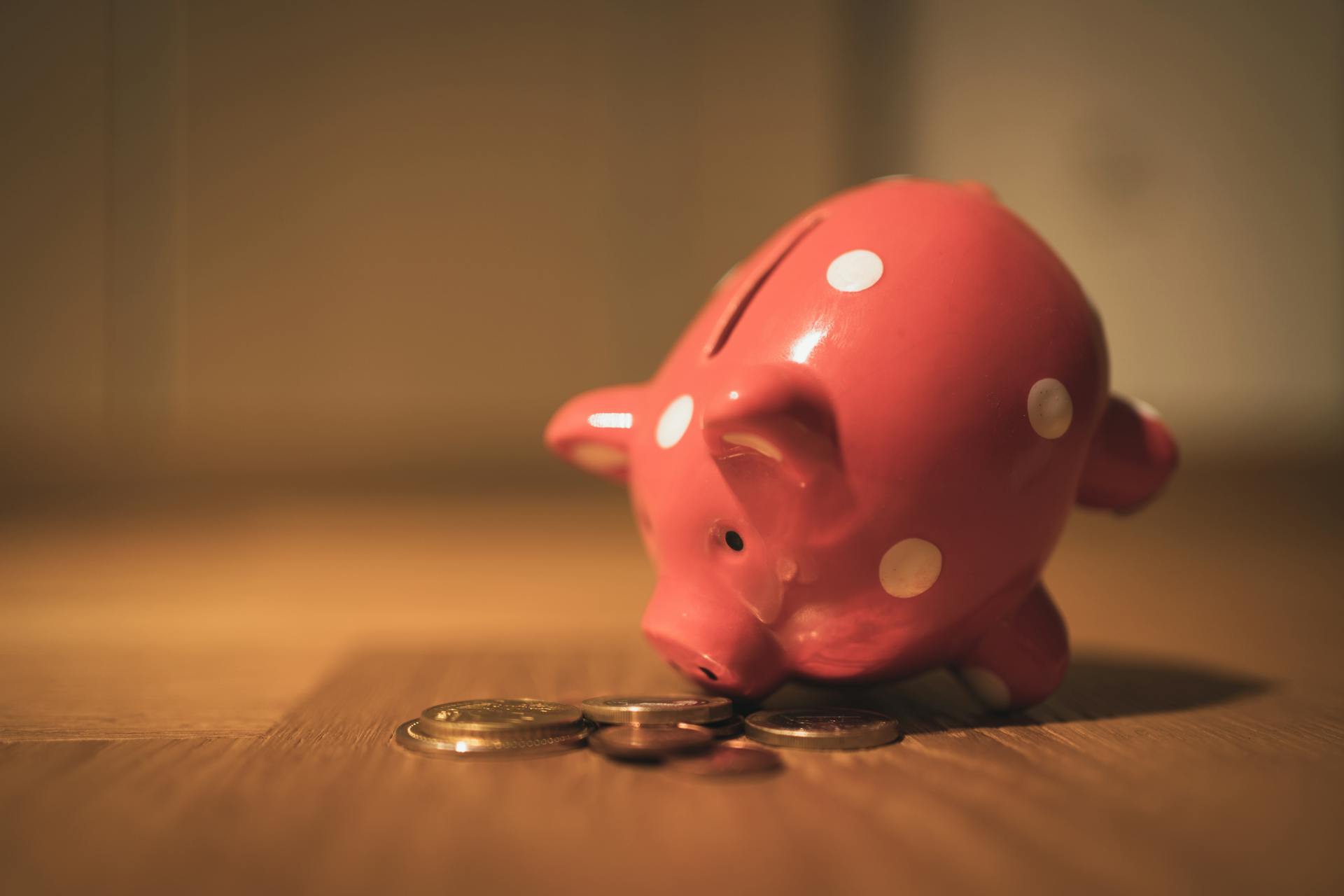 A red ceramic piggy bank with polka dots surrounded by coins, symbolizing savings and finance.