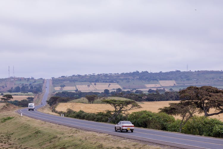 Cars Driving On Asphalt Road Surrounded With Fields