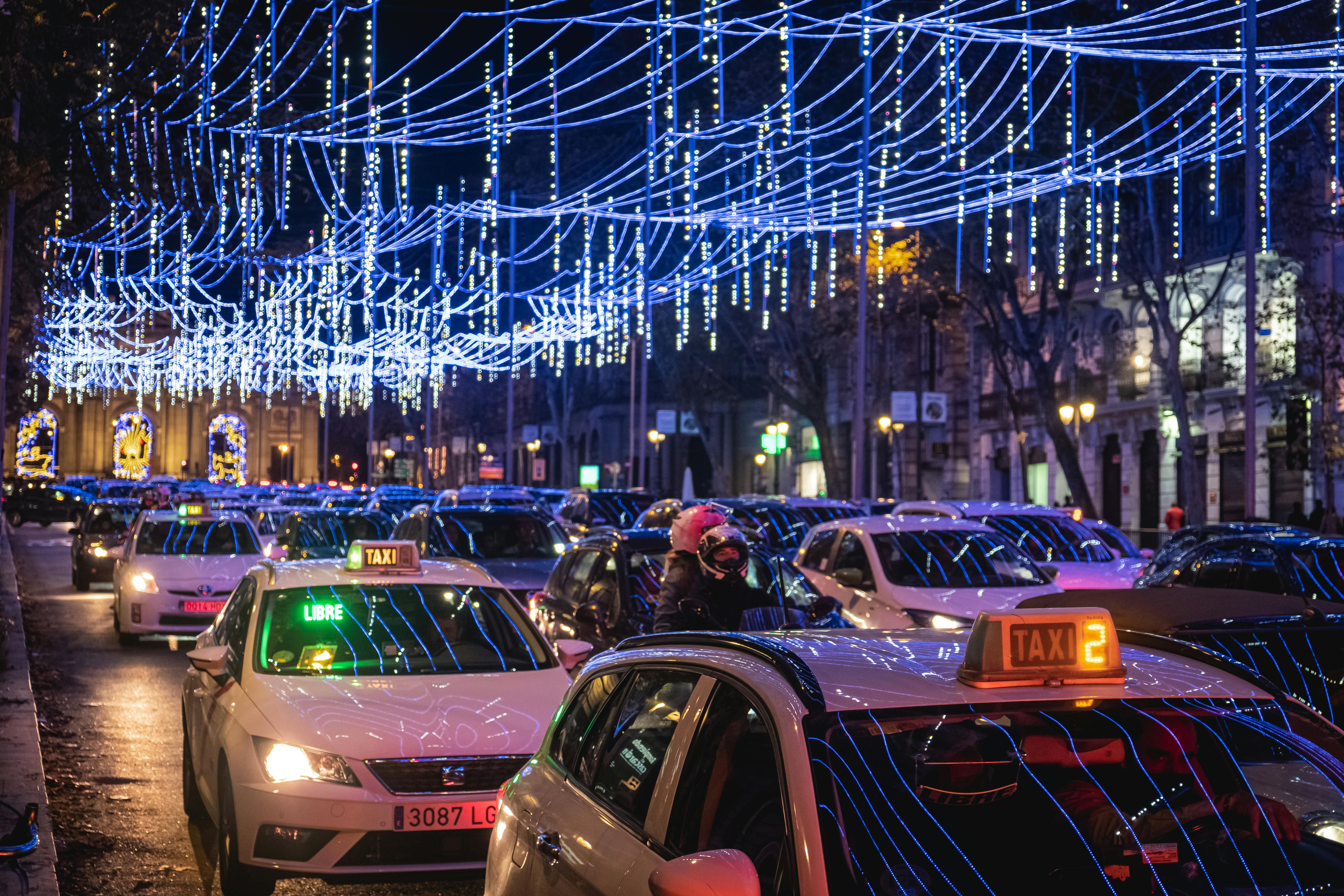 Vibrant city street in Madrid featuring taxis under festive Christmas lights at night.