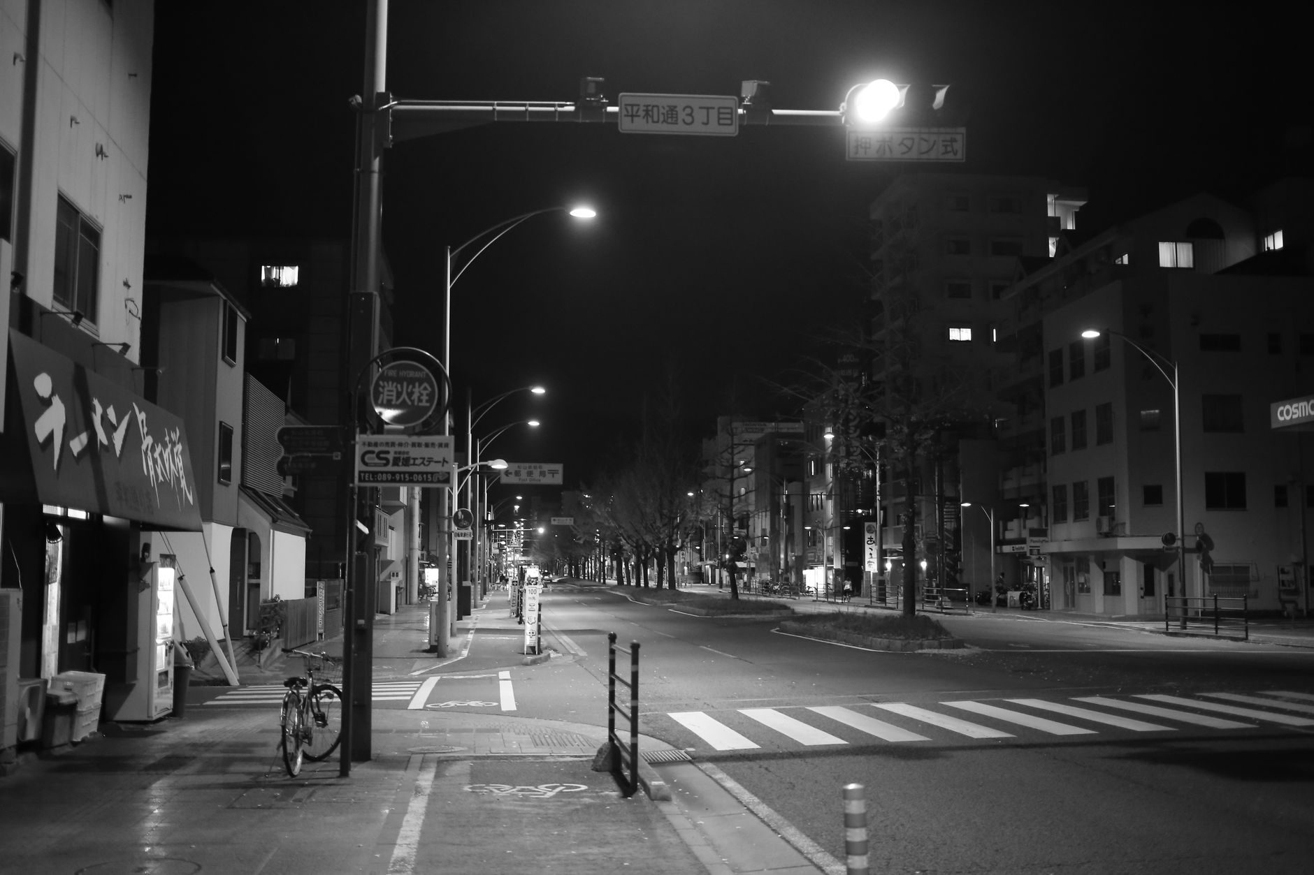 A tranquil city street at night, captured in black and white, showcasing urban architecture and streetlights.