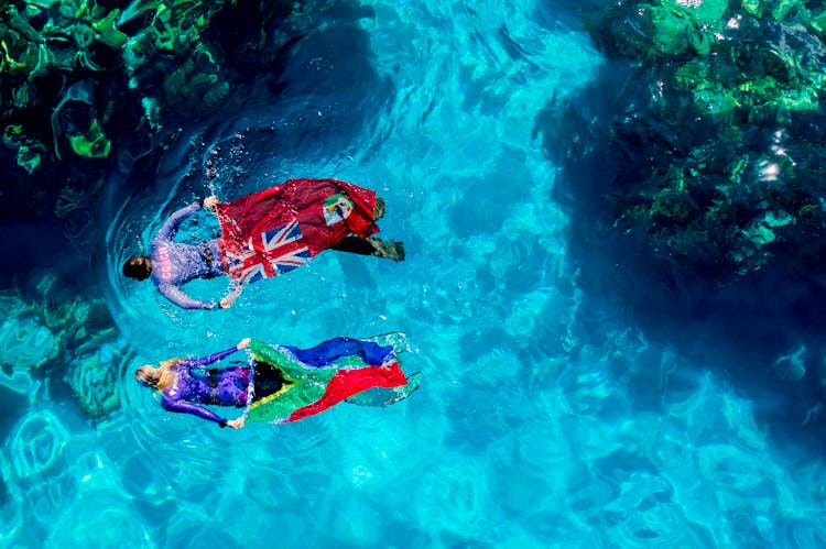 People In Swimwear Holding Flags Swimming In Water