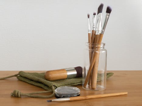 Set of eco-friendly makeup brushes in a glass jar on a wooden table, showcasing sustainable beauty tools.