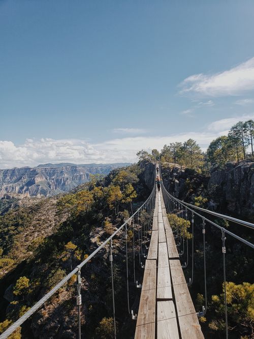 Free A scenic wooden suspension bridge stretches across a stunning mountain landscape under a clear sky. Stock Photo