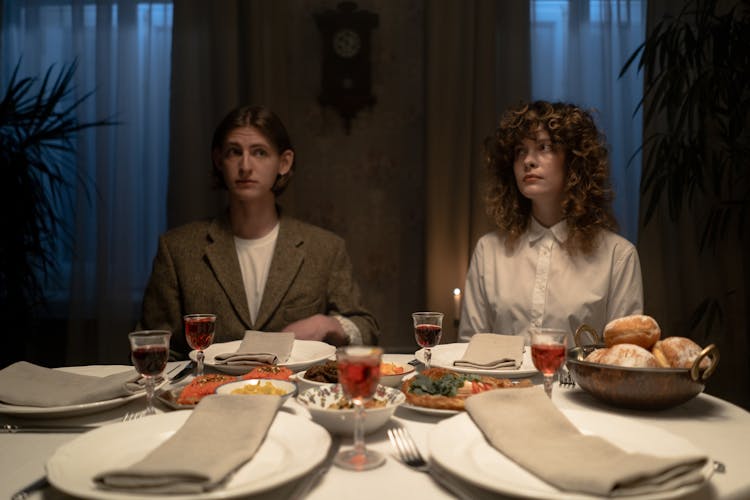 Man And Woman Seated In Front Of A Table With Food