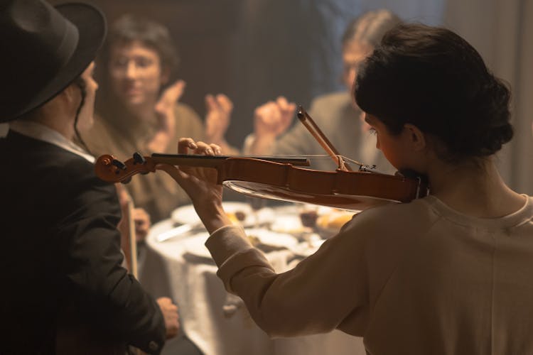 Woman Playing Violin At A Dinner Table During Hanukkah Celebration