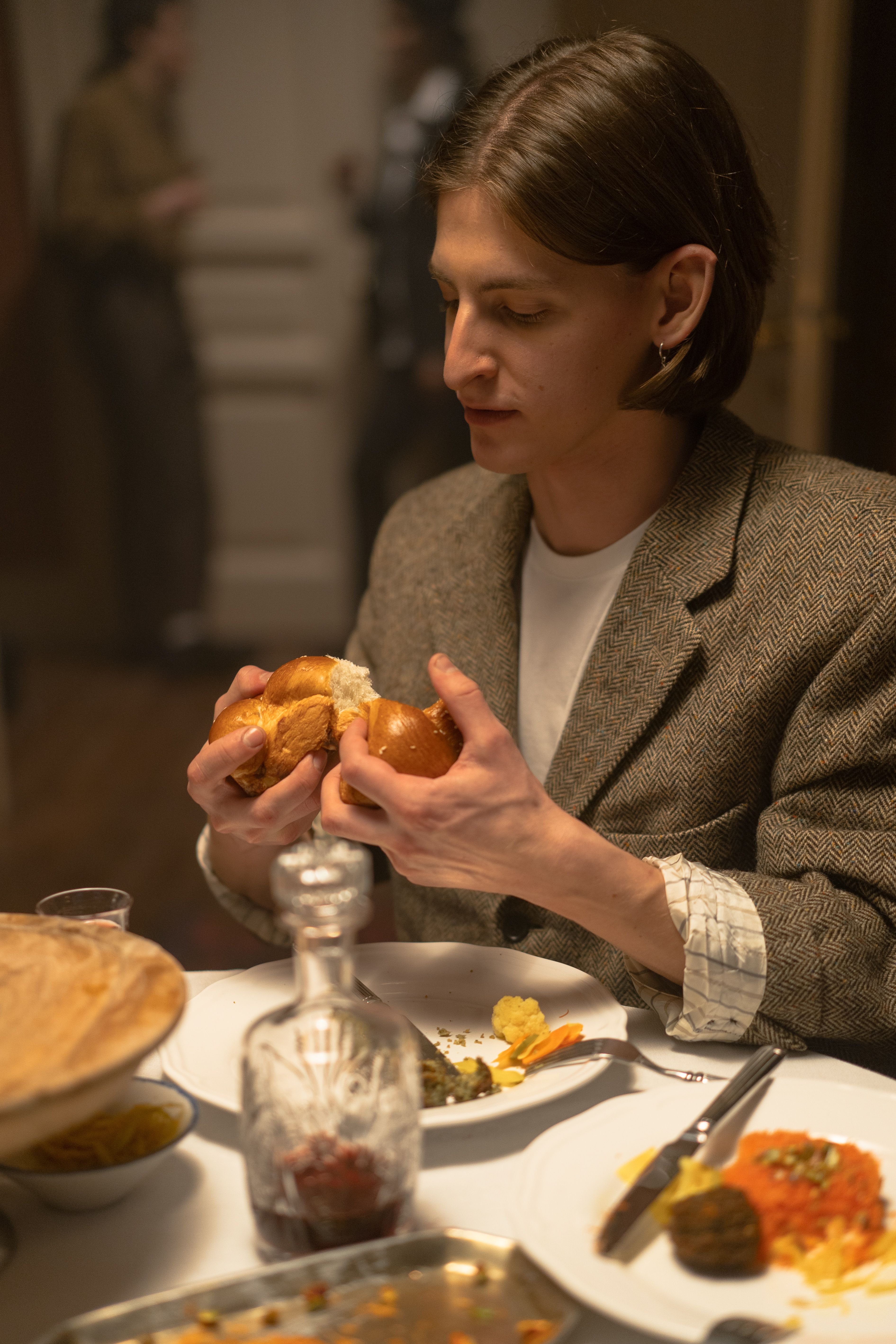 A young man enjoys a traditional meal indoors, breaking bread at a festive dinner table.
