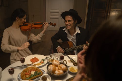 Man And Woman Playing Musical Instruments At A Dinner Table 