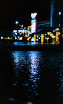 Moody nighttime street scene featuring wet pavement reflecting city lights.