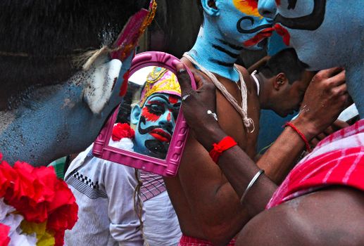 A vibrant cultural scene featuring face-painted individuals reflected in a handheld mirror, showcasing traditional adornments.