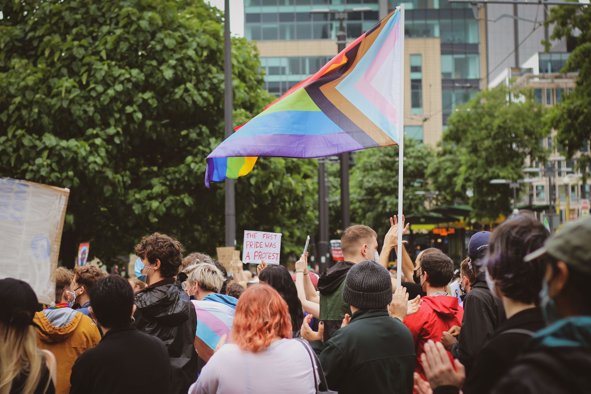 Şehirde bir yürüyüşte Progress Pride bayrağı ve bir pankart taşıyan maskeli göstericiler