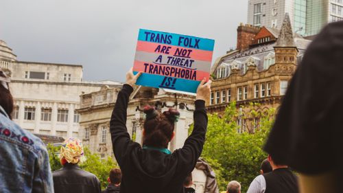 Free Protest scene with a sign advocating against transphobia in an urban setting. Stock Photo