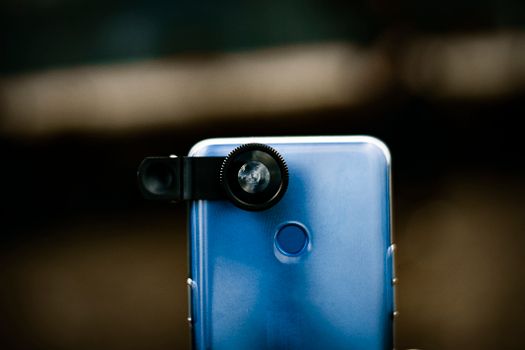 Zoom optical lens attached to camera of modern smartphone against blurred background in daytime