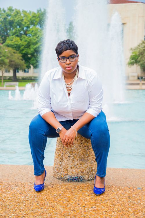 Free Stylish woman wearing eyeglasses and pearl necklace sitting by a water fountain. Stock Photo