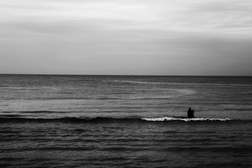 Grayscale Photo of Person Fishing in the Ocean