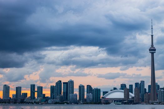 Dramatic view of Toronto's skyline and CN Tower against a cloudy sunset sky.