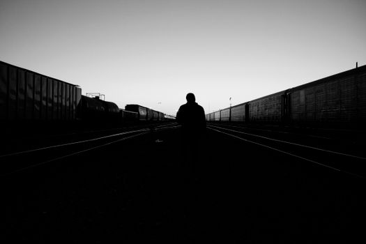 Moody black and white photo of a lone silhouette walking along empty railway tracks at dusk.