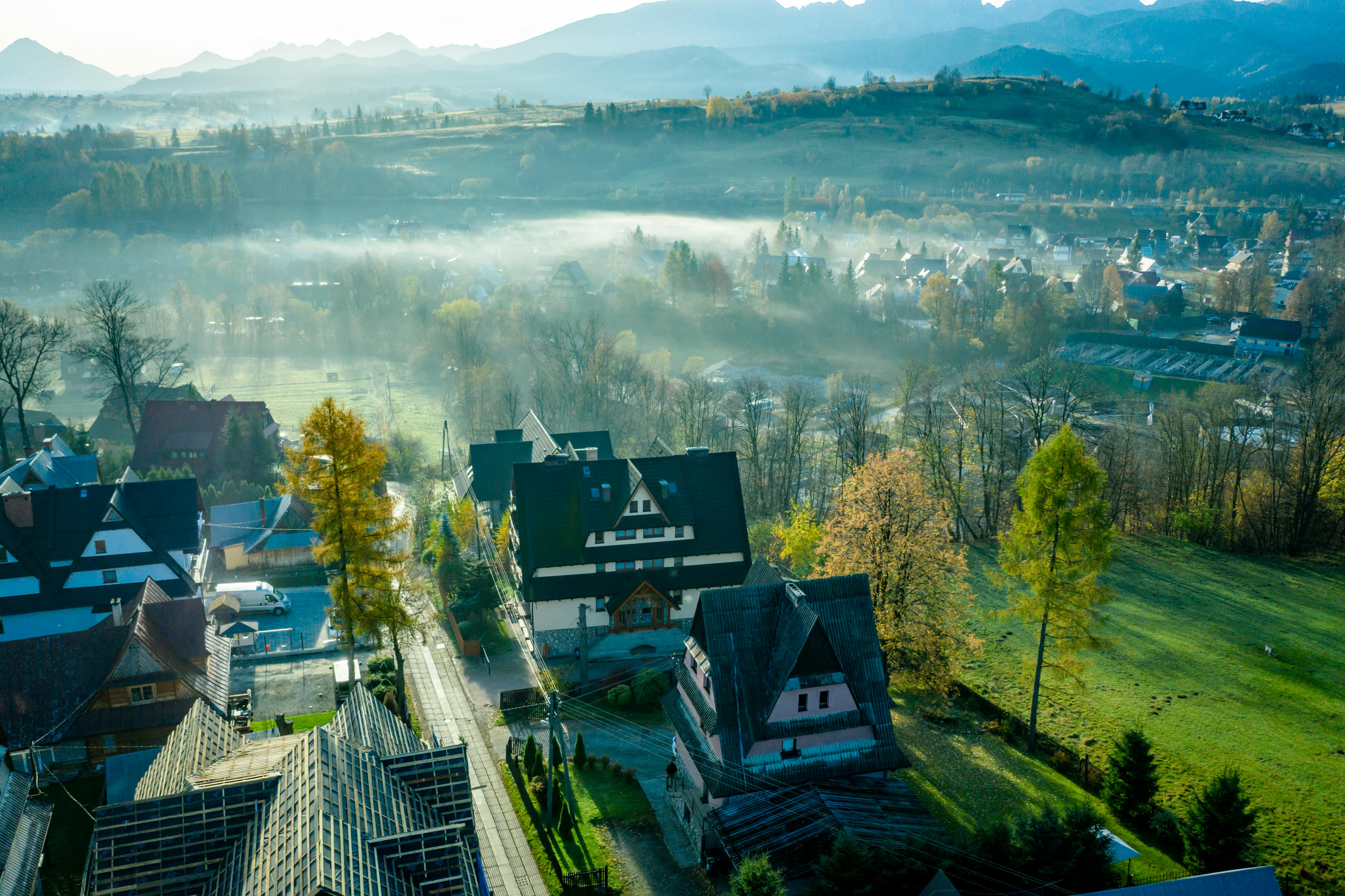 Aerial view of Zakopane with fog covering the landscape, traditional houses, and vibrant autumn colors.