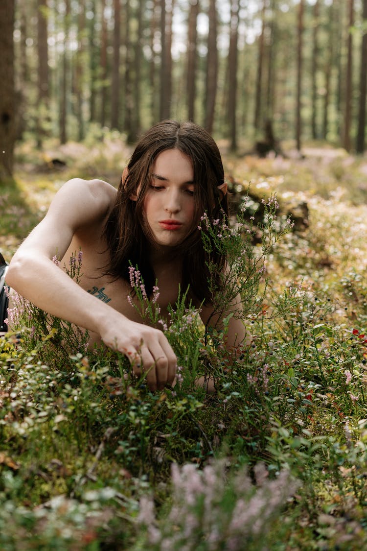 Man With Long Hair Picking Up Flowers In The Woods