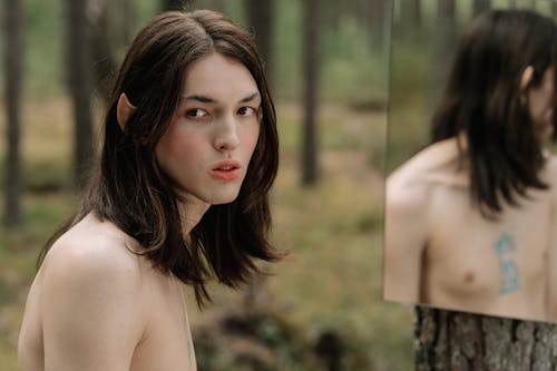 Shirtless Man with Long Hair Standing in Front of a Mirror