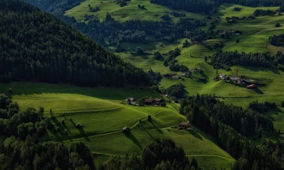 Aerial view of lush green hills, forests, and small villages in a picturesque countryside setting.