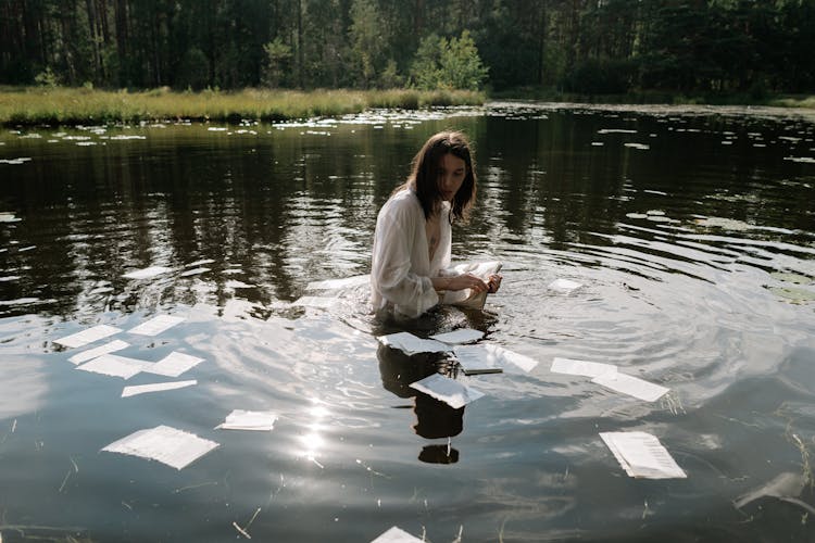 A Person Wearing White Long Sleeves Tearing The Pages Of A Book While Soaking In The Lake