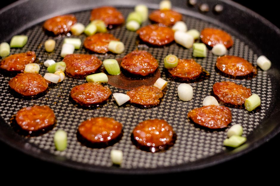 Thick pink slices of Taylor Ham pork roll browning and curling slightly in a cast iron skillet, with crisp caramelized edges forming around each slice.