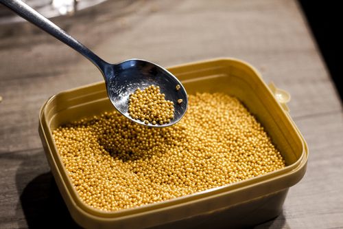 Free Plastic container placed on gray table filled with small golden sprinkle balls with spoon above Stock Photo