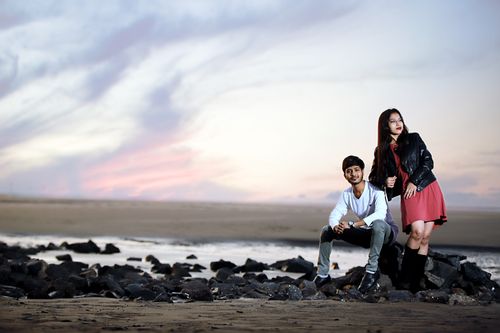 Free Young couple posing stylishly on a rocky beach at Surat, India during sunset. Stock Photo