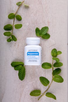 Top view of a peppermint essential oil bottle surrounded by fresh mint leaves.