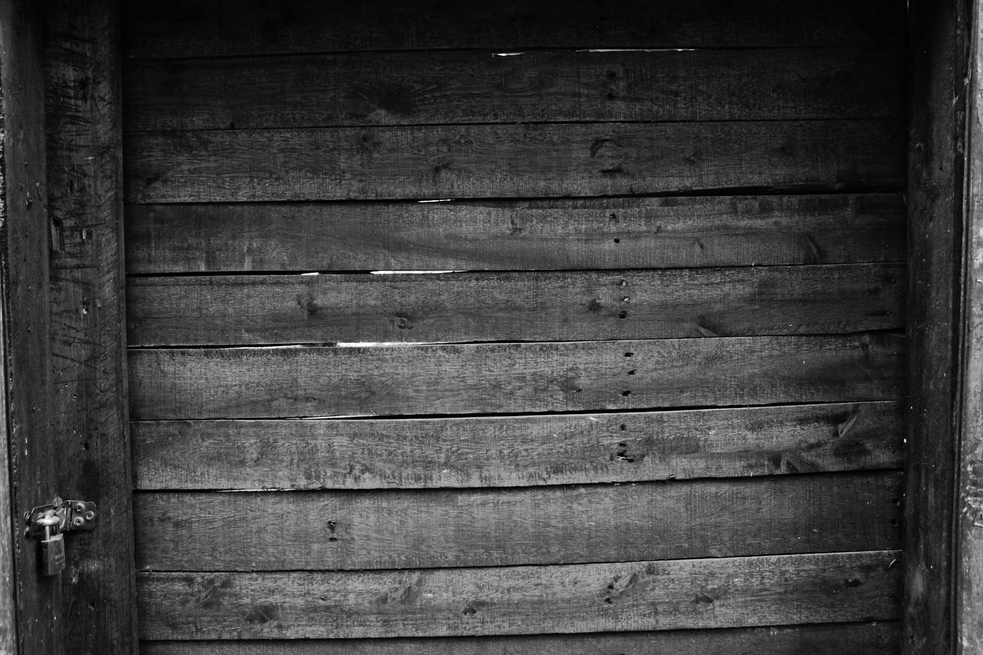 Black and white photo of a locked vintage wooden door, showcasing rustic textures.