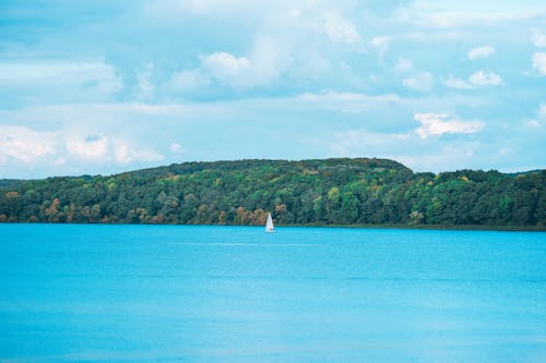 View Of Lake With Sailboat Under A Cloudy Sky