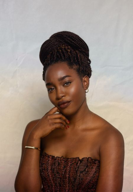 Attractive African American female wearing accessories and casual clothes with bare shoulders on colorful background with hand at chin