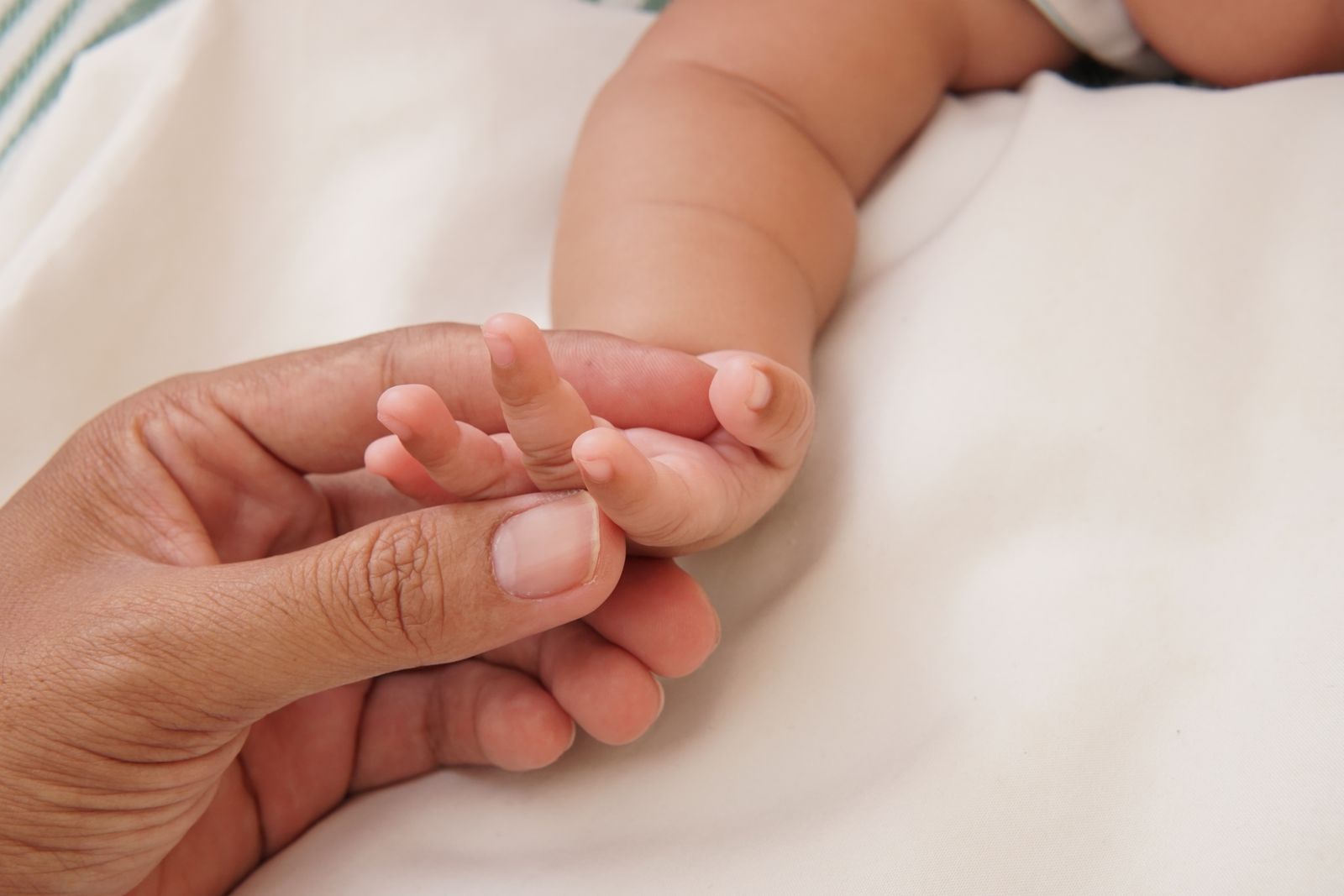A newborn's tiny hand wrapped around a parent's finger