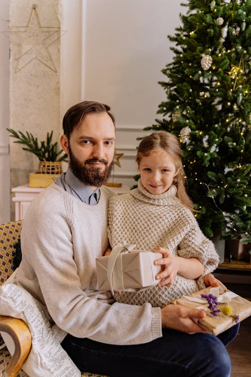 Father and Daughter Sitting Near A Christmas Tree Holding Gifts