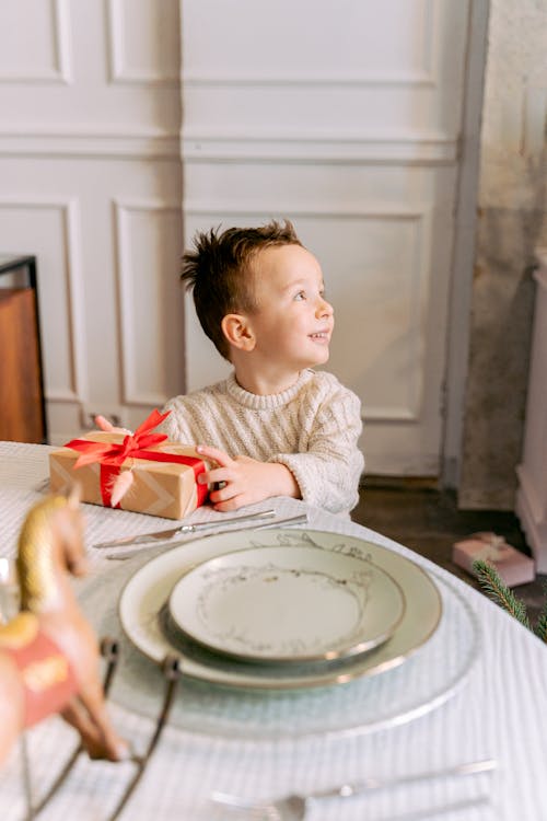 Free Child in White Sweater Standing By The Table With A Gift Stock Photo