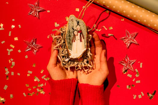 Hands holding a handmade festive Christmas ornament on a red background with stars and confetti.