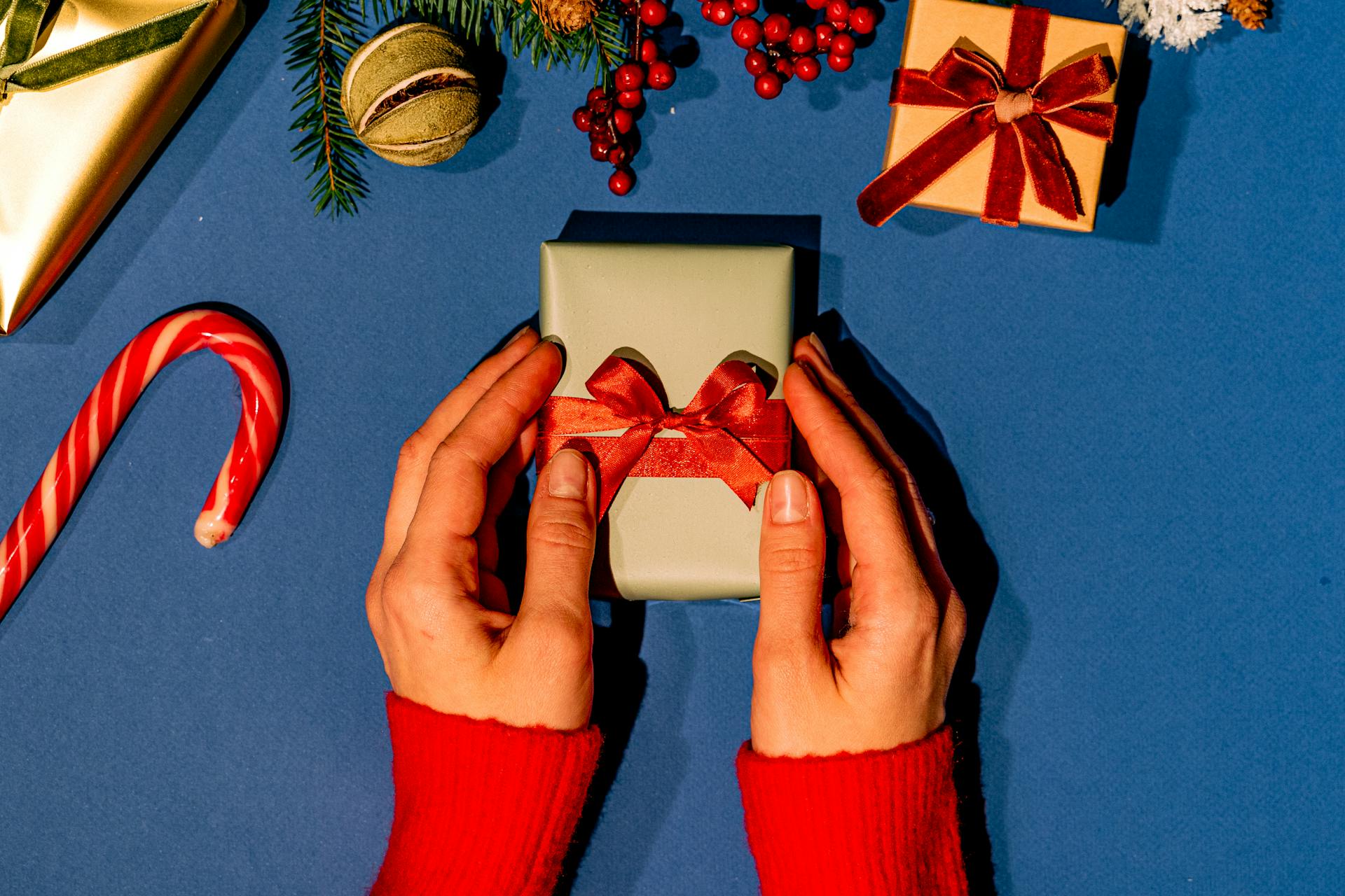 Hands Holding Gift Box with Red Ribbon