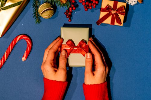 Free Hands holding a Christmas gift with red ribbon on a blue surface, surrounded by festive decorations. Stock Photo