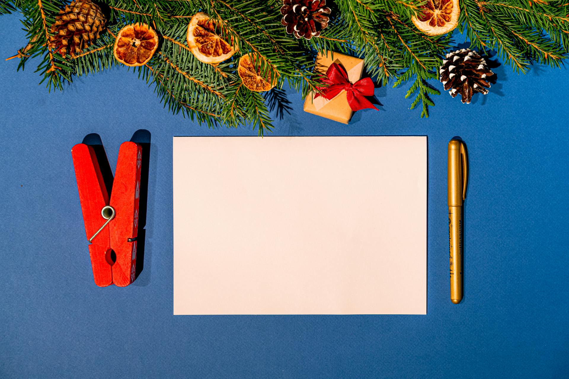 Top-down view of a festive Christmas card mockup with pine branches, ornaments, and gift box on a blue background.