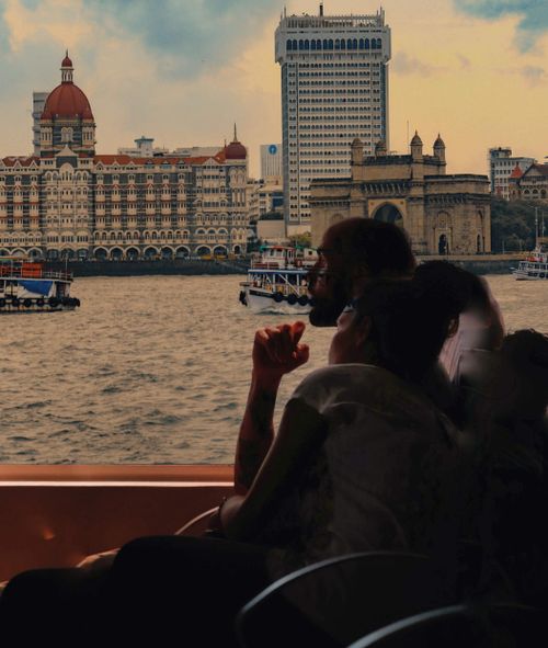 Free Side view of couple sitting on passenger seats of ship floating on rippling sea with vessels near historical buildings on embankment Stock Photo