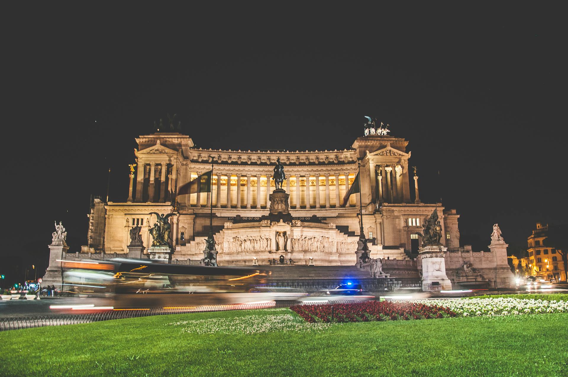 Exterior of Victor Emmanuel II National Monument or Vittoriano located in Rome in Italy at night with green grass and flowers nearby