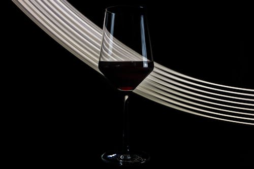 Wineglass of fragrant exquisite red wine placed against black background with white shiny lines